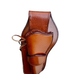 May include: A brown leather holster with a glossy finish. The holster features a curved design with a flap closure and a loop for securing. The leather has a rich, warm tone, suggesting a handcrafted item.
