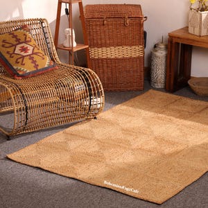 May include: A rectangular natural fibre rug with a geometric design, shown in a room setting. The rug has a woven texture. A wicker chair and storage basket are also visible, suggesting a bohemian or rustic decor style. The text "BohemianRugzCafe" is visible.
