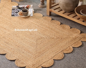 May include: A natural jute rug with a scalloped edge. The rug is a light tan colour and has a woven texture. The rug is on a grey surface. The text "BohemianRugzCafe" is visible on the rug.