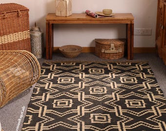 May include: A rectangular area rug featuring a repeating geometric pattern in dark charcoal and cream. The design consists of interlocking star-like shapes and central squares. The rug has a short fringe along the bottom edge and a flat weave.