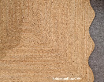 May include: A natural jute rug with a scalloped edge and a square corner design. The rug is a light tan colour and has a woven texture. The text "BohemianRugzCafe" is visible on the edge of the rug.