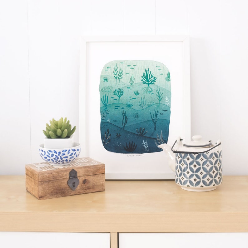 May include: A framed watercolor print of an underwater scene with a gradient of blue and green colors. The print features various types of seaweed, fish, and coral. The print is titled "Nathalie Bertrand".