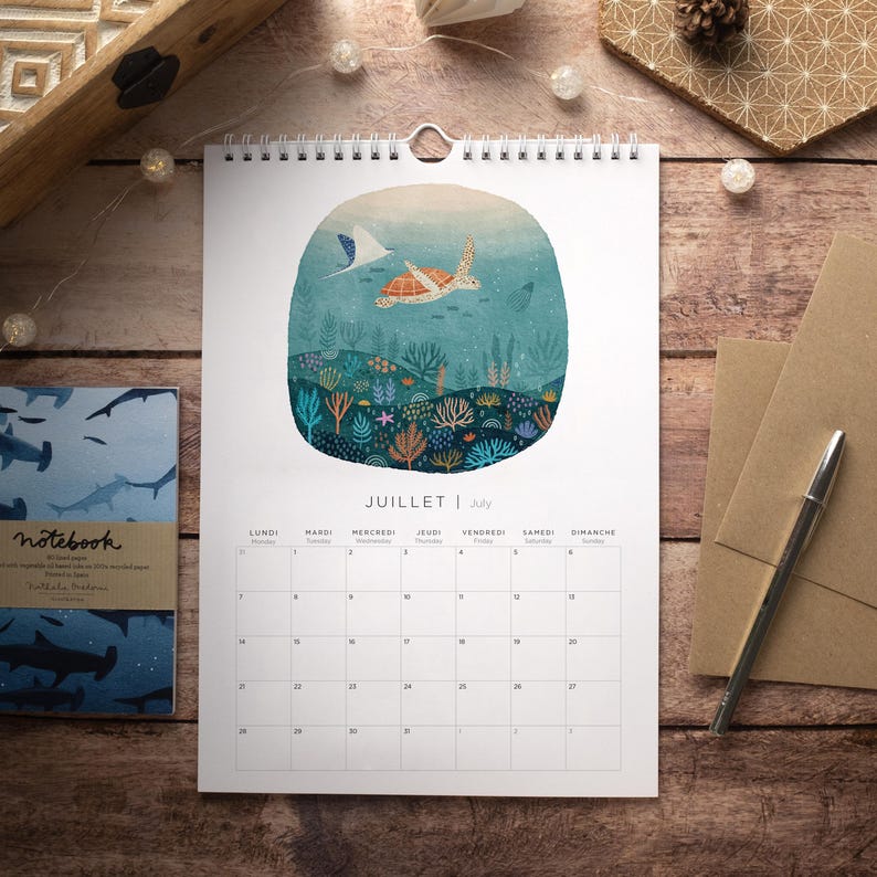 May include: A white calendar with a colorful illustration of a sea turtle swimming in an underwater scene. The calendar is for July and has the French word "JUILLET" printed on it.