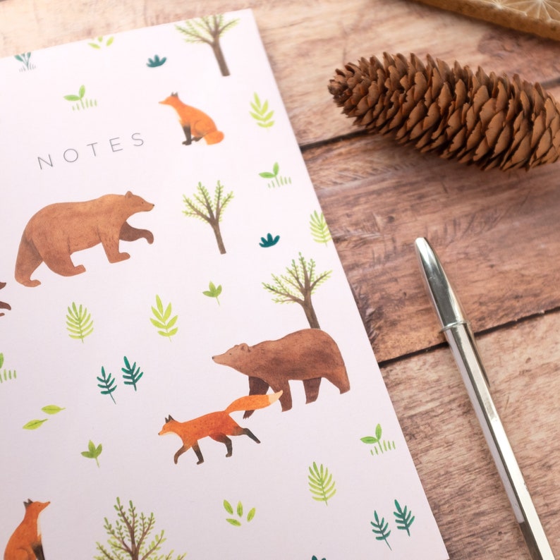 May include: A pink notebook with the word "NOTES" printed on the front. The notebook has a woodland theme with illustrations of bears, foxes, and trees.