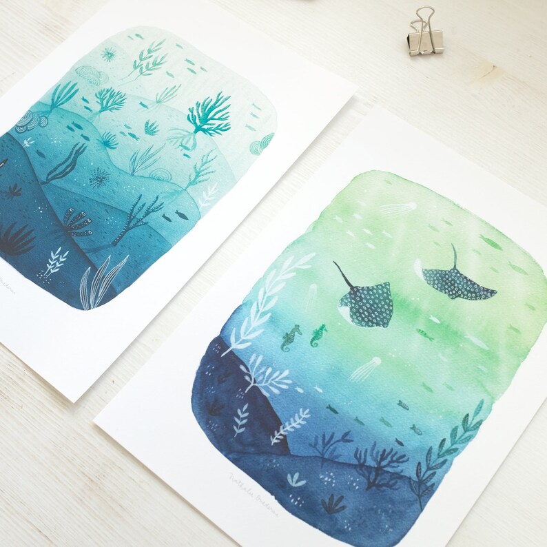May include: Two watercolor prints depicting underwater scenes. The first print features a blue and green gradient with various sea life, including seaweed, coral, and fish. The second print features a green and blue gradient with two manta rays swimming in the water, along with seahorses and jellyfish.