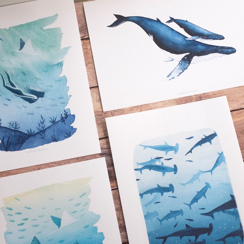 May include: Four watercolor paintings of ocean life. The first shows a mermaid swimming in a blue and green ocean. The second shows a humpback whale and a calf swimming in a blue ocean. The third shows a school of fish swimming in a blue and yellow ocean. The fourth shows a school of hammerhead sharks swimming in a blue ocean.