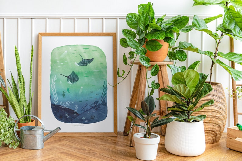 May include: A framed watercolor illustration of two stingrays swimming in a blue and green ocean. The illustration is surrounded by houseplants in terracotta and white pots.