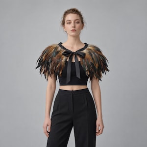 May include: A shoulder-covering feather capelet featuring layered natural brown, black, and tan feathers. The garment is secured at the front with a black satin ribbon tie that forms a bow, resting over a black cropped top and black trousers.