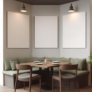 May include: A restaurant dining area with a square wooden table, two wooden chairs, and a built-in bench with green cushions. Three blank white framed canvases hang on the wall. Two pendant lights illuminate the scene.