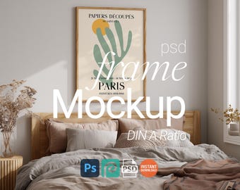 May include: A framed art print with the text "PAPIERS DÉCOUPÉS PARIS" hangs above a bed with neutral-toned bedding. The artwork features a yellow sun and green shapes. The image includes the words "frame Mockup" and "DIN A Ratio".
