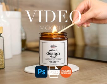 May include: A lit candle in a brown glass jar with a white label that says "your design here". The candle sits on a white coaster. The text "VIDEO MOCKUP" is at the top of the image. The candle is being lit with a match.