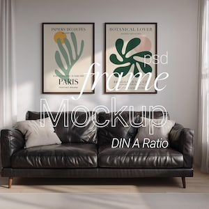 May include: A living room scene featuring a black leather sofa with two throw pillows, beneath two framed art prints. The prints have a beige background with abstract shapes in green, pink, and yellow. The text on the prints reads "PAPIERS DÉCOUPÉS PARIS" and "BOTANICAL LOVER".