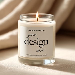 May include: A burning candle in a clear glass jar with a white label. The label says "CANDLE COMPANY" above "your design here" in black text. The candle is 100% soy and has a burn time of 40 hours.