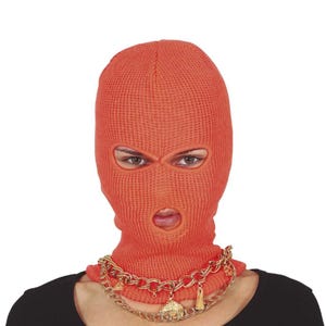 Może przedstawiać: Pomarańczowa dzianinowa kominiarka z otworami na oczy i usta. Kominiarka jest noszona ze złotym łańcuszkiem z zawieszkami. Osoba ma na sobie czarny top.