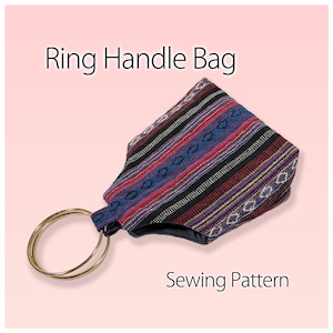 Pode incluir: Um molde de costura para bolsa com alças de argola em tecido com padrão de riscas multicoloridas em vermelho, azul, preto e branco. A bolsa tem duas argolas metálicas douradas como alças. O texto "Ring Handle Bag" e "Sewing Pattern" é visível.