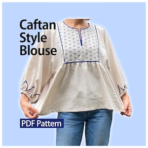 Op de afbeelding: Een beige blouse in caftan-stijl met een blauw bloemenpatroon op de borst, een split-halslijn en blauwe zigzag-afwerking op de mouwen. De tekst "Caftan Style Blouse" en "PDF Pattern" is zichtbaar. De blouse heeft wijde mouwen.