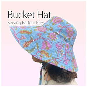 Può includere: Un cappello a secchio blu con un motivo floreale rosa e verde. Il cappello ha un'ampia tesa e un sottogola. Il testo sull'immagine recita "Bucket Hat Sewing Pattern PDF".