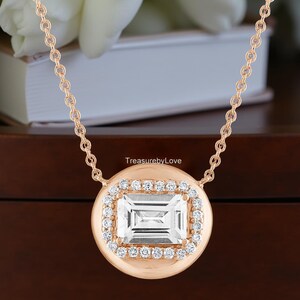 May include: Rose gold necklace featuring a rectangular, clear gemstone surrounded by a halo of smaller, clear gemstones. The pendant is suspended from a delicate rose gold chain. The necklace is displayed against a soft background.