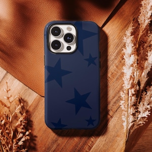 Puede incluir: Funda de teléfono azul marino con un patrón de estrellas azul oscuro. La funda se muestra sobre una superficie de madera con un fondo de cuero y plantas secas. La funda está diseñada para un teléfono inteligente.