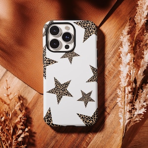 May include: White phone case with a leopard print star pattern. The case has a black camera lens border and a glossy finish. The stars are a tan and brown color, and the background is white.