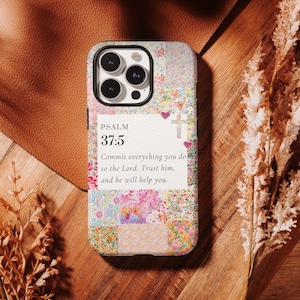 May include: A floral patterned phone case with the text "PSALM 37:5" and a religious quote. The case features a patchwork design with pink, white, and green floral patterns. A cross and hearts are also visible.