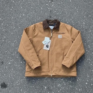 Puede incluir: Chaqueta de trabajo marrón con cuello de pana marrón, cremallera frontal y un pequeño parche cuadrado con el logotipo en el pecho. La chaqueta tiene dos bolsillos delanteros y una etiqueta adjunta. La chaqueta está hecha de un material duradero.