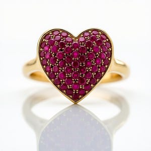 May include: A gold ring featuring a heart-shaped design. The heart is encrusted with numerous small, round, deep red gemstones. The ring's band is a simple, polished gold, and the gemstones are set closely together, creating a solid, vibrant heart shape.