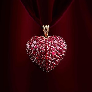 May include: A heart-shaped pendant necklace, densely covered in red gemstones, hangs from a burgundy velvet ribbon. The pendant's gold bail contrasts with the deep red of the gems and ribbon, creating a luxurious and romantic aesthetic.