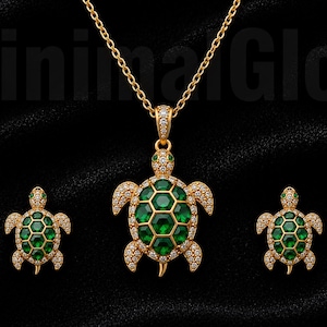 May include: A gold-toned jewellery set featuring a turtle pendant on a chain and matching turtle earrings. Each piece displays a central shell made of hexagonal green stones, surrounded by small clear pavé crystals and green stone eyes.