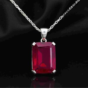 May include: A silver necklace with a large, rectangular, ruby-red gemstone pendant. The pendant is set in a silver frame and hangs from a delicate silver chain. The background is a dark, solid color.