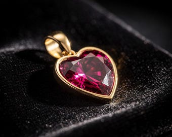May include: A heart-shaped pendant with a vibrant red gemstone set in a gold frame. The pendant is suspended from a gold bail, and the gemstone has multiple facets. The jewelry is displayed on a black velvet surface.