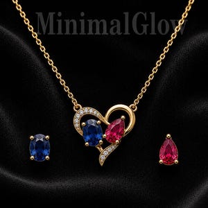 May include: A gold necklace and earring set featuring the text MinimalGlow. The heart-shaped pendant contains an oval blue stone and a pear-shaped red stone with small clear accents. One earring is an oval blue stone and the other is a pear-shaped red stone.
