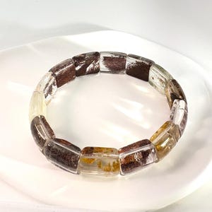 May include: A quartz bracelet featuring rectangular beads with brown and yellow inclusions. The bracelet is presented on a white surface. Each bead is approximately 1.5 cm in length, showcasing the natural patterns.