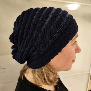 May include: A dark navy blue knit beanie hat with a ribbed design. The hat has a folded brim and a textured, striped pattern. The hat is made of a soft, knitted material and is designed to be worn on the head.