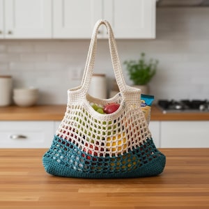 May include: A cream-colored, crocheted tote bag with a teal base and filled with fresh fruit. The bag has a net-like design and sturdy handles. The bag is sitting on a wooden surface.