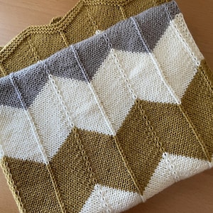 Puede incluir: Dos mantas de punto con un patrón de chevrón. Una manta es principalmente de color amarillo mostaza con rayas de chevrón blancas y grises. La otra manta es de color amarillo mostaza. Las mantas están hechas de un hilo suave y texturizado.