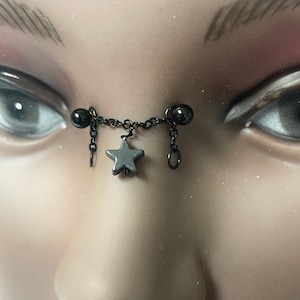 May include: Black nose piercing with a star charm and two black beads. The piercing is on a mannequin.
