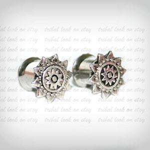 May include: A pair of silver ear gauges with a starburst design. The gauges have a smooth, polished finish and feature a detailed starburst pattern with a central circle.