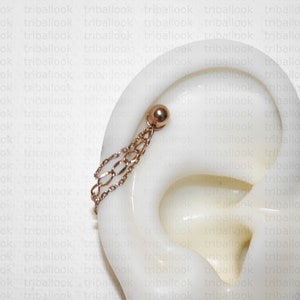 K&ouml;nnte beinhalten: Ein goldener Kettenohrring mit einem kleinen goldenen Kugelanh&auml;nger. Der Ohrring h&auml;ngt an einem Ohrmodell.