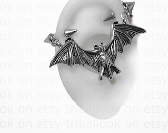 Peut inclure: Boucle d'oreille en argent en forme de chauve-souris avec des pointes. La chauve-souris est en vol, les ailes déployées. La boucle d'oreille est conçue pour être portée sur la partie supérieure de l'oreille.