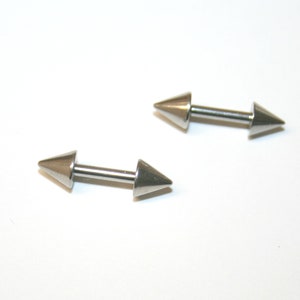 May include: Two silver barbell style body piercing jewellery pieces with pointed ends.