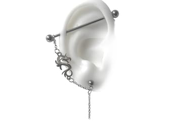 Peut inclure: Barbell industriel argenté avec une chaîne pendante et un charme de dragon. Le barbell est inséré dans l'oreille d'un mannequin.