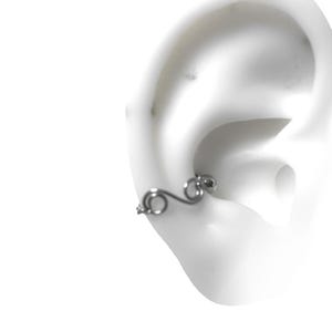 May include: Silver ear cuff with a curved design and a small circle detail. The cuff is shown on a model's ear.