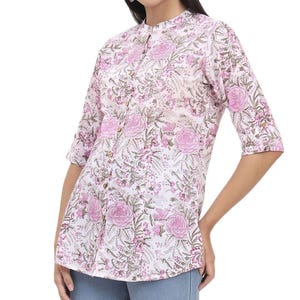 May include: A light pink floral print shirt with a mandarin collar and three-quarter sleeves. The shirt features a button-down front and a delicate pattern of pink roses and green leaves on a white background. The shirt is made of a lightweight fabric.