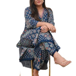 May include: A two-piece navy blue outfit with a floral pattern. The top has long sleeves and a V-neckline with a pink trim. The matching pants have a cropped length. The outfit is worn with clear sandals.