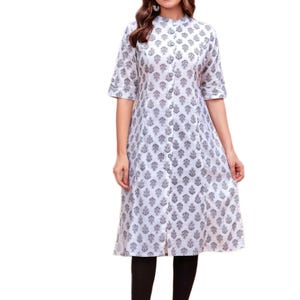 Peut inclure: Robe blanche mi-longue avec un col mandarin et des manches courtes. La robe présente un motif floral gris répété et un devant boutonné. La robe est portée avec des leggings noirs.