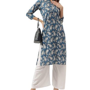 Peut inclure: Un haut tunique à imprimé cachemire bleu sarcelle avec des manches trois-quarts et un col mandarin. Le haut est associé à un pantalon palazzo blanc. Un sac à main noir est tenu dans la main gauche. La tenue convient aux tenues décontractées ou semi-formelles.