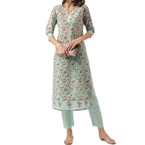 May include: A two-piece floral print outfit in a light teal color. The outfit includes a long tunic with three-quarter sleeves and matching pants. The floral pattern features red flowers and green leaves. A pink clutch is held in the hands.