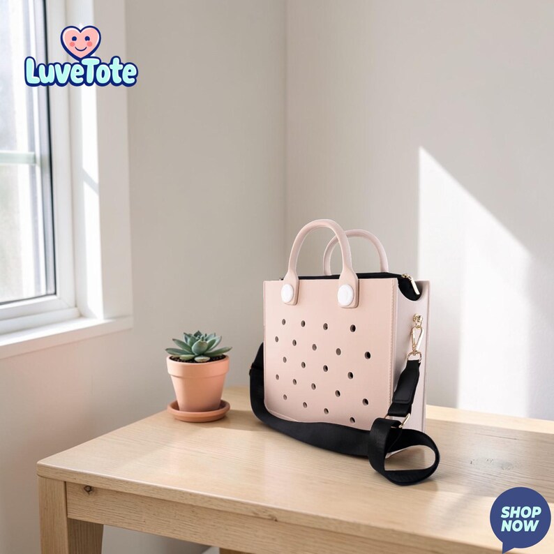 May include: A light pink tote bag with a black shoulder strap and handles. The bag has a perforated design and a zipper closure. A small potted succulent sits on a wooden table next to the bag. The brand name "Luvetote" is visible in the upper left corner.