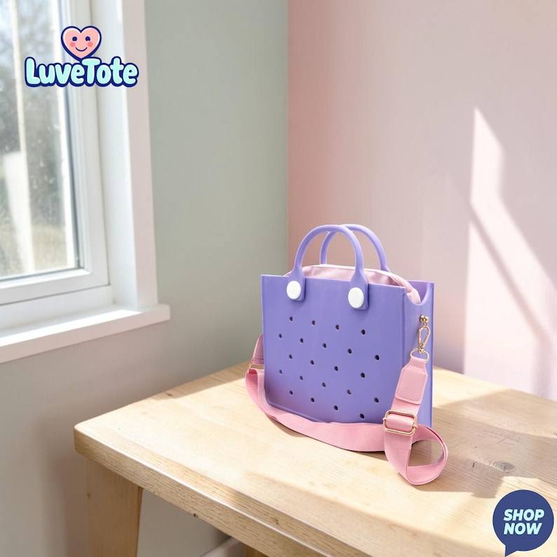 May include: A lavender tote bag with a pink interior and strap. The bag has a perforated design and white handle accents. The bag is on a wooden table with a window and wall in the background. The text "Luvetote" is in the upper left corner.